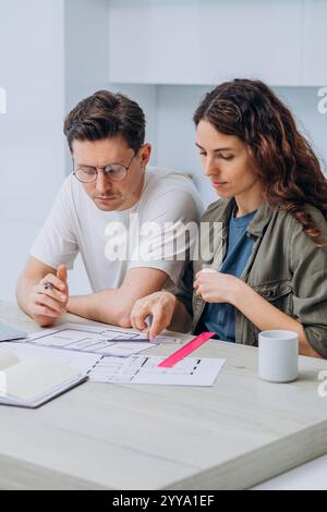 Due architetti si sono impegnati in una discussione su un progetto di casa, analizzando i progetti sparsi sul tavolo utilizzando un righello e una matita per perfezionare il loro design e migliorare i dettagli Foto Stock