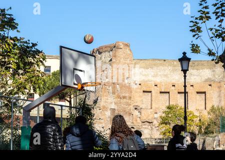 Roma, Italia - 15 novembre 2024: Ragazzi che giocano a basket sul campo del Parco del Colle Oppio, con le rovine delle Terme di Traiano sullo sfondo Foto Stock