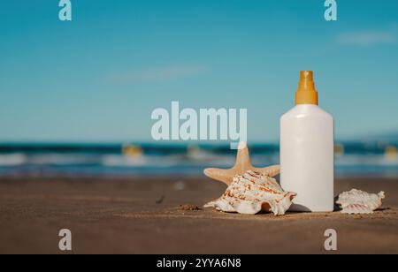 Bottiglia di crema solare sulla spiaggia sabbiosa con conchiglie e stelle marine sotto il cielo azzurro Foto Stock
