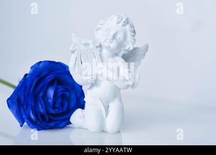 Statuetta cherubina con rosa blu su sfondo bianco Foto Stock