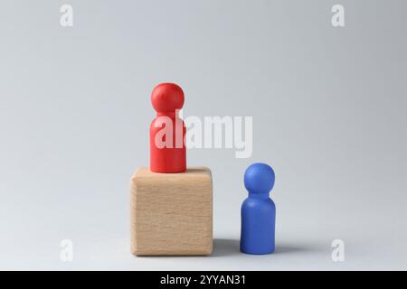 Concetto di concorrenza. Figura umana su cubo di legno e un altro dietro su sfondo chiaro Foto Stock