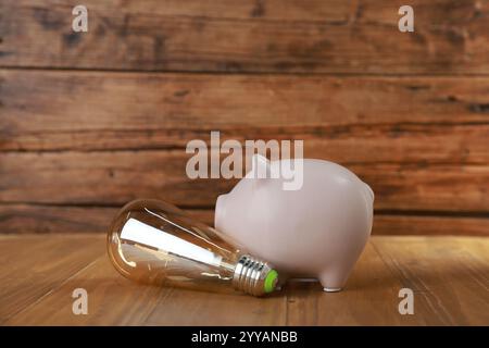 Salvadanaio e lampadina su un tavolo di legno. Concetto di risparmio energetico Foto Stock