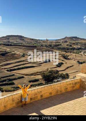 Una donna in camicia gialla nella Cittadella storica di Victoria e una vista sull'area circostante dell'isola di ​​Gozo nella giornata di sole, Malta Foto Stock