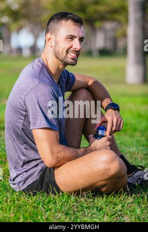 Vista laterale uomo sorridente che riposa sull'erba dopo l'allenamento. Verticale Foto Stock