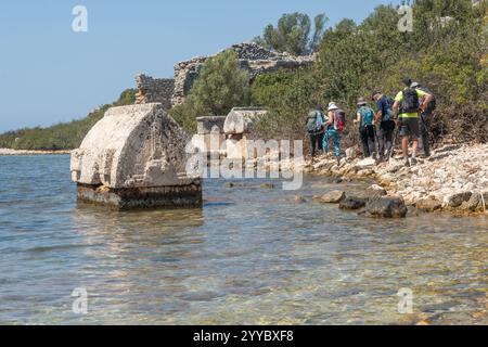 Gli esploratori attraversano le antiche rovine lungo la tranquilla costa, scoprendo la ricca storia della zona. Foto Stock