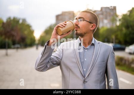 Ritratto di un giovane uomo d'affari che sta in piedi per strada e beve caffè per andare. Foto Stock