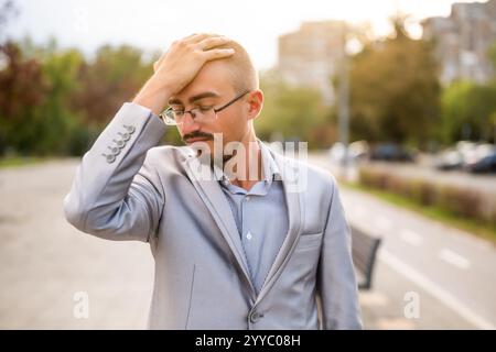 Ritratto di un giovane uomo d'affari ansioso e scontento che si trova in strada. Uomo d'affari esausto e deluso dopo il lavoro. Foto Stock