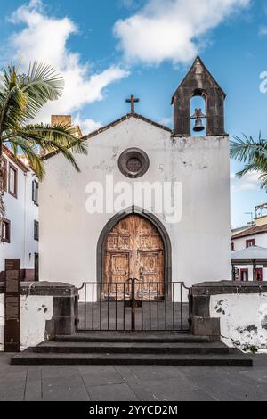 Un'affascinante facciata rustica della chiesa con porte in legno, un campanile e circondato da palme sotto un cielo azzurro luminoso, che crea un ambiente tranquillo e rilassante Foto Stock