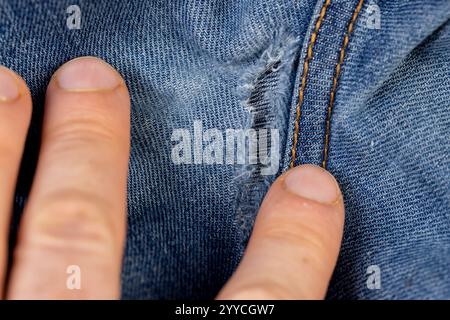 vecchi jeans strappati da usura frequente, jeans danneggiati con un foro nel tessuto adatto per la riparazione e cuciture da vicino Foto Stock