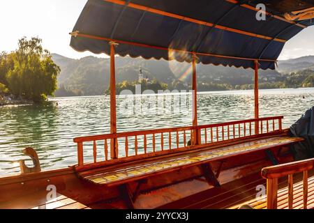 Barca turistica in legno che naviga sul lago dissanguato in slovenia, mostrando l'iconica chiesa dell'isola sullo sfondo di montagne Foto Stock