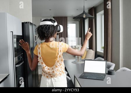 Vista posteriore dell'irriconoscibile donna che imposta l'app VR per una casa intelligente mentre sei in piedi in cucina Foto Stock