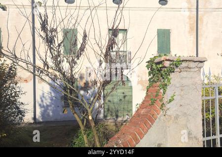 Facciata di un maniero abbandonato in un villaggio nella campagna italiana visto da dietro una recinzione in pietra Foto Stock