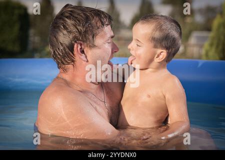 Un paio di uomini e un bambino si rinfrescano durante la giornata calda nella piscina del giardino Foto Stock