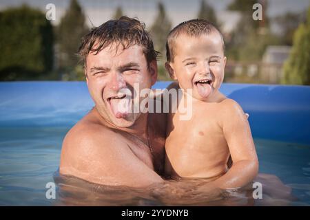 Un paio di uomini e un bambino si rinfrescano durante la giornata calda nella piscina del giardino Foto Stock