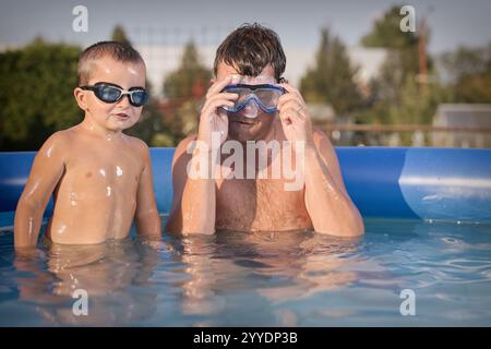 Un paio di uomini e un bambino si rinfrescano durante la giornata calda nella piscina del giardino Foto Stock