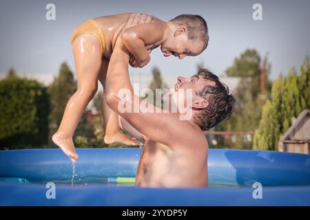 Un paio di uomini e un bambino si rinfrescano durante la giornata calda nella piscina del giardino Foto Stock