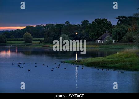Lago Blagdon con casa bianca e nera sul lago, preso all'alba con un lampo di colore nel cielo che si riflette sul lago e numerosi bir d'acqua Foto Stock