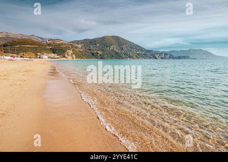 Acque cristalline turchesi che si lavano delicatamente sulle sabbie dorate di una spiaggia tranquilla, sostenuta da lussureggianti colline verdi, la quintessenza della tranquillità Foto Stock