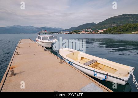 24 ottobre 2024, Tivat, Montenegro: Due motoscafi attraccano in un molo di cemento sulla costa adriatica, con una pittoresca cittadina e montagne Foto Stock