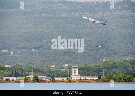 24 ottobre 2024, Tivat, Montenegro: Aereo passeggeri bianco decollo sopra la torre di controllo dell'aeroporto vicino al mare con verdi colline sullo sfondo Foto Stock