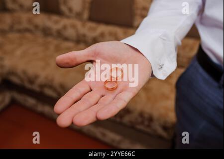 Due anelli di nozze dorati tenuti in mano a uno sposo prima della cerimonia. Foto Stock