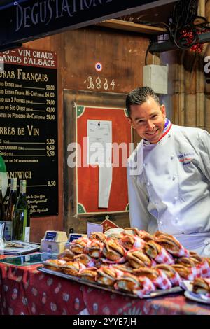 Strasburgo, Francia - 13 dicembre 2024: Il famoso Chef Gilles Reinhardt del ristorante Paul Bocuse serve panini di foie gras al mercato di Chrismas Foto Stock