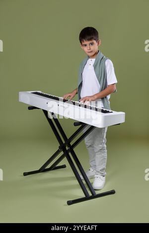 Ragazzo carino che suona sintetizzatore su sfondo verde oliva Foto Stock