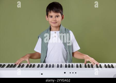 Ragazzo carino che suona sintetizzatore su sfondo verde oliva Foto Stock