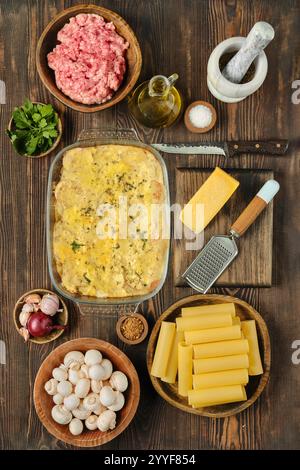 Carne macinata fresca, verdure e spezie disposte intorno a una deliziosa casseruola di pasta al forno in un ambiente accogliente in cucina Foto Stock