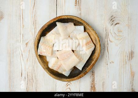 Una ciotola di legno riempita di filetti di pesce bianco freschi e tagliati si trova su un piano in legno rustico, ideale per cucinare. Il pesce sembra invitante e letto Foto Stock
