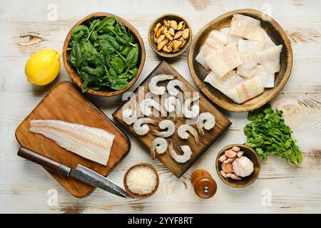 Vista dall'alto degli ingredienti freschi, tra cui gamberi, pesce, spinaci, limone e cozze disposti su tavole di legno Foto Stock