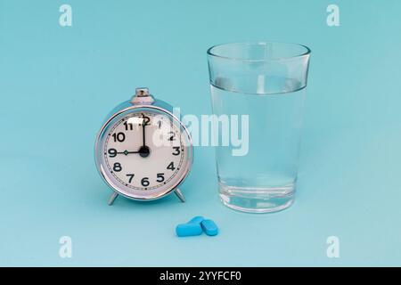 Sveglia con pillole e un bicchiere d'acqua su sfondo blu Foto Stock
