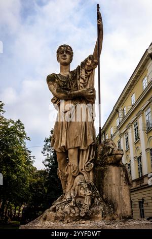 Una statua di un uomo con una lancia è in piedi di fronte a un edificio. La statua è fatta di pietra e ha un aspetto molto antico e intempestivo. Il bui Foto Stock