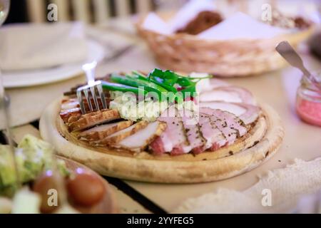 Un piatto di cibo con una varietà di carni e verdure su un asse di legno. Il piatto è appoggiato su un tavolo con altri piatti e utensili Foto Stock