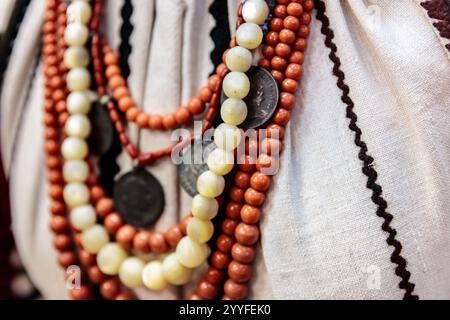 Viene mostrata una collana con perline e monete. La collana è fatta di perline bianche e rosse e ha una moneta d'oro al centro. La collana è indossata da un per Foto Stock