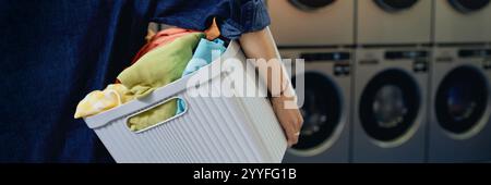 Immagine dell'intestazione del sito Web di una donna irriconoscibile che trasporta un cesto con un bucato sporco che prepara vestiti colorati per il lavaggio in lavanderia automatica a gettoni, spazio per le copie Foto Stock