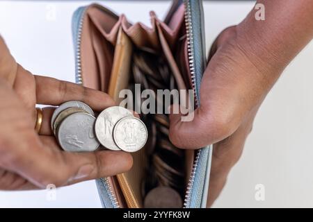 Mani che tengono monete in rupia indiana con un portafoglio pieno di monete. Primo piano, finanza, concetto di valuta. Foto Stock