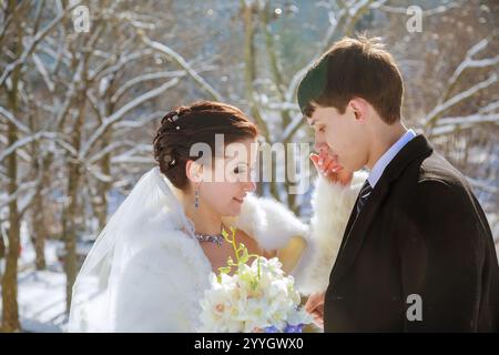 Gli sposi sposi si uniscono nel paese delle meraviglie invernali, circondati da alberi innevati la sposa regala un bouquet di fiori bianchi e condividono un momento tenero. Foto Stock