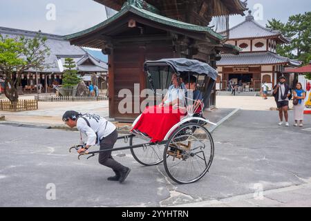 Miyajima, Giappone - 20 giugno 2024: I turisti esplorano la via dello shopping Miyajima Omotesandō, in arickshaw o jinrikisha, situata vicino all'Itsukushima Jinj Foto Stock
