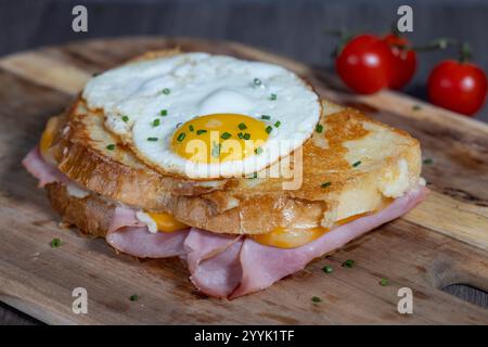 Croque Madame o formaggio alla griglia con prosciutto e uovo su un tagliere di legno. Il panino è tostato e ha un tuorlo che cola Foto Stock