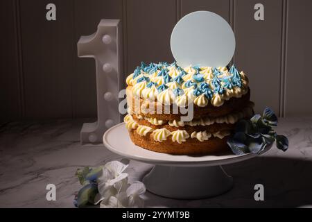 Una torta del primo compleanno con spazio per il testo su un disco sopra la torta. Un singolo numero è sulla tavolozza a lato. una torta bianca. Foto Stock