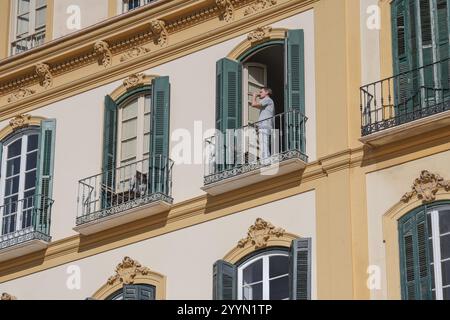 Un giovane in piedi sul balcone di un edificio che beve qualcosa da una bottiglia, Plaza de la Merced, Malaga, Andalusia, Spagna, Europa Foto Stock