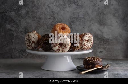 Un banco per torte con un'ampia selezione di piccole ciambelle decorate, un piatto laterale contiene una ciambella a scelta con una forchetta d'oro. Foto Stock