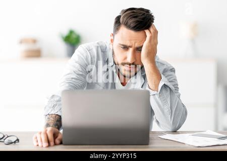 Stress freelance. Il freelance maschile si stanca dopo aver lavorato su un notebook a casa, avendo problemi con il progetto, seduto sul posto di lavoro Foto Stock