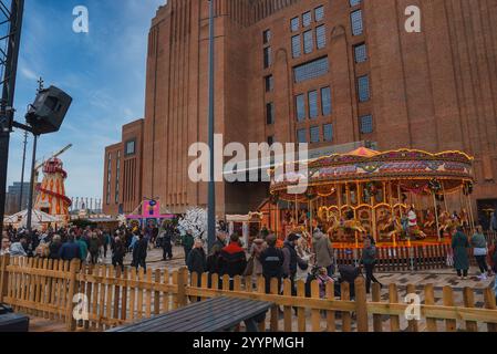 L'immagine mostra un vivace mercatino di Natale fuori dalla Tate Modern a Londra, con una giostra, uno skelter e folle che si godono il bancomat festivo Foto Stock