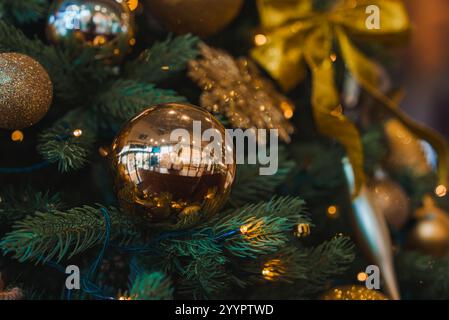 Un albero di Natale a Londra è decorato con ornamenti, luci scintillanti e nastri d'oro. Un baule dorato riflette l'ambiente circostante, aggiungendo un tou unico Foto Stock