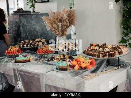 Elegante esposizione di dessert con torte assortite, frutta ed elementi decorativi. Foto Stock