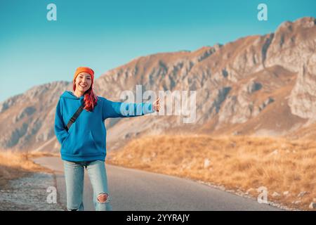 L'autostop turistico su una strada panoramica di montagna mostra un gesto di pollice in alto Foto Stock