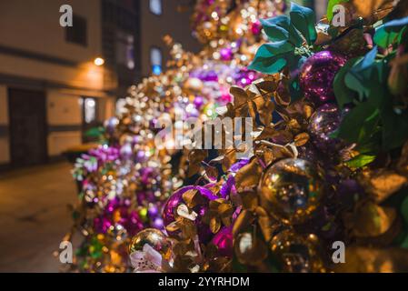 Un primo piano di un albero di Natale decorato a Londra, caratterizzato da foglie dorate, baubles viola e oro, con una strada delicatamente illuminata sullo sfondo. Foto Stock