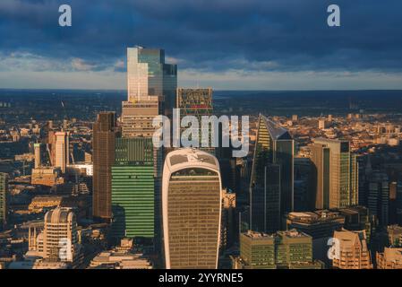 L'iconico skyline di Londra presenta gli edifici Walkie Talkie e Leadenhall, inondati di luce dorata contro un cielo buio e nuvoloso durante il Natale Foto Stock